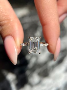 a woman's hand holding an engagement ring with a large emerald stone in it