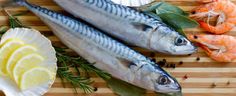 two fish on a cutting board next to lemons, garlic and parsley with other food items