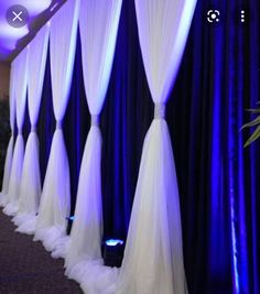 rows of white drapes are lined up in front of a blue curtained wall