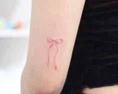 a woman's arm with a small pink bow tattoo on the left side of her arm