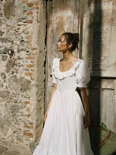 a woman wearing a white dress standing in front of an old building with a basket