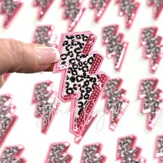 a hand holding a pink and black cheetah lightning bolt sticker in front of a white background