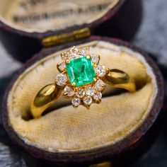 an emerald and diamond ring in a wooden box with its lid open to show it's inside