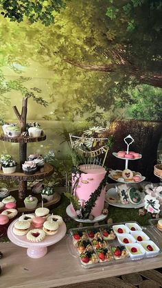 a table topped with cakes and desserts next to a forest wallpapered wall