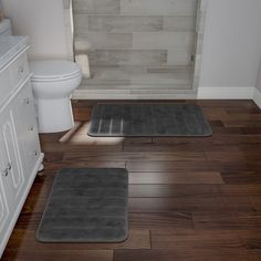 two bath mats sitting on top of a wooden floor next to a toilet and sink