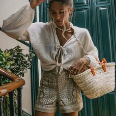 a woman wearing sunglasses and holding a basket in front of a green door with stairs