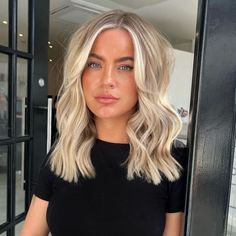 a woman with blonde hair standing in front of a glass door and looking at the camera