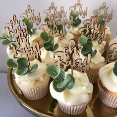 cupcakes with white frosting and green leaves are on a gold platter