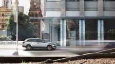 a car is driving down the street in front of a building with tall buildings and trees