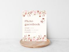 a photo guest book on a wooden stand next to a white wall with pink flowers