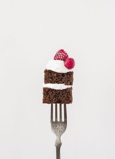 a piece of cake on a fork with white frosting and raspberries