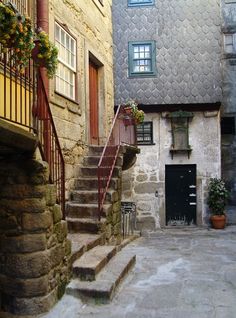 an alleyway with stone buildings and steps leading up to the door, potted plants on either side