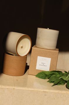 two candles are sitting on top of a box and some green leaves next to it