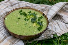 a wooden bowl filled with broccoli soup on top of a checkered cloth