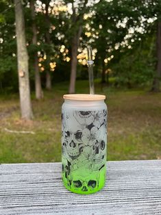 a green cup with a straw in it sitting on top of a wooden table next to trees