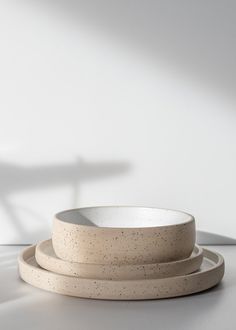 three white bowls sitting on top of each other next to a shadow cast object in the background