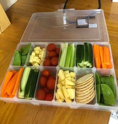 a plastic container filled with lots of different types of vegetables next to crackers and tomatoes