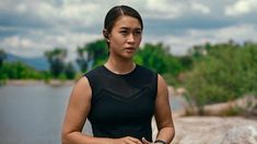 a woman standing in front of a body of water wearing a black top and bracelet