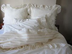 an unmade bed with white linens and ruffled pillow cases on the headboard