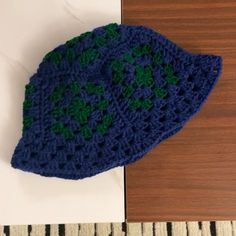 a blue and green crocheted hat sitting on top of a wooden table next to a white wall