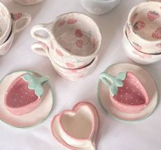 a table topped with dishes and cups filled with strawberry shaped bowls, saucers and spoons