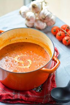 a pot of tomato soup on a red towel next to some tomatoes and cloves