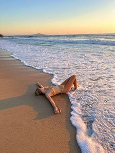 a woman laying on top of a sandy beach next to the ocean