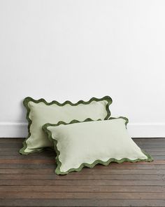 two green scalloped pillows sitting on top of a wooden floor next to a white wall