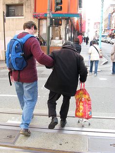 two people are walking down the street with bags on their backs and one person is pulling luggage behind them