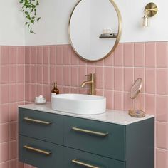 a bathroom with pink and green tiles on the walls, gold fixtures and a round mirror