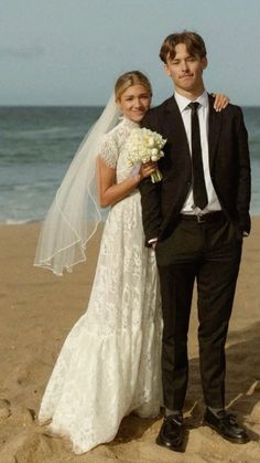 a bride and groom pose for a photo on the beach in front of the ocean