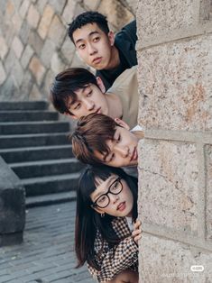 three people leaning against a stone wall with their heads on each other's shoulders