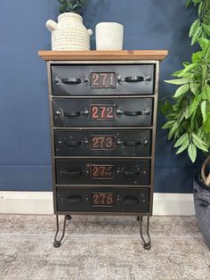 an old dresser with drawers and numbers on the front is next to a potted plant