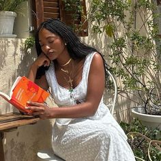 a woman sitting on a bench reading a book and holding an orange box in her hand