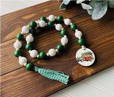 a green and white beaded necklace with a tasseled charm sits on top of a wooden table