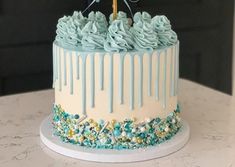 a birthday cake with blue icing and gold decorations on the top is sitting on a table