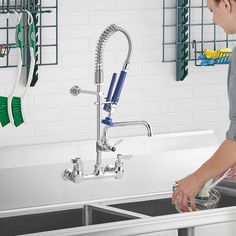 a woman washing dishes in a kitchen sink with green and blue brushes on the faucet