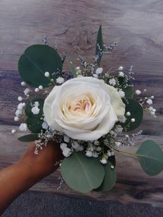 a white rose and baby's breath bouquet in someones hand on a wooden surface