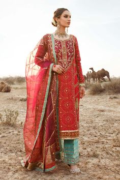 a woman standing in the desert wearing a red and blue outfit with gold details on it