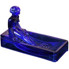 a blue glass figurine is sitting in a boat shaped like a person on the water