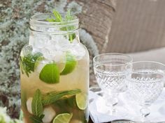 a mason jar filled with ice and limes on top of a table next to two glasses