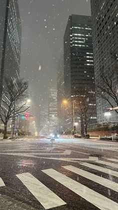 a city street at night with snow falling on the ground and tall buildings in the background