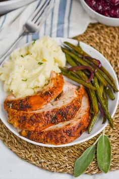 a white plate topped with meat, mashed potatoes and green beans next to a bowl of cranberry sauce