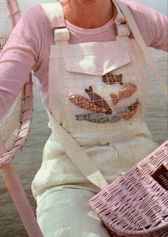 a woman sitting on a boat holding a basket and wearing an apron with fish embroidered on it