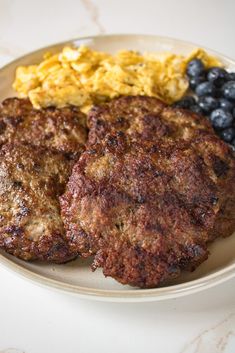 two hamburger patties, scrambled eggs and blueberries on a plate