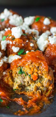 meatballs covered in marinara sauce and feta cheese on a black plate with green garnish