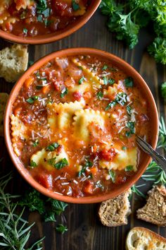 two bowls of pasta soup with bread and parsley on the side next to it