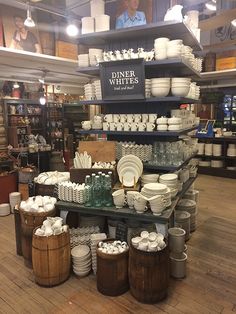 a display in a store filled with lots of white dishes and cups on top of wooden barrels