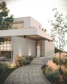 a woman standing in the doorway of a modern house with stone steps leading up to it