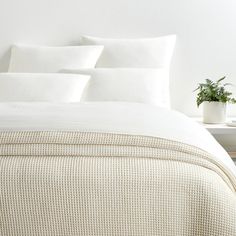 a bed with white sheets and pillows on top of it next to a small potted plant